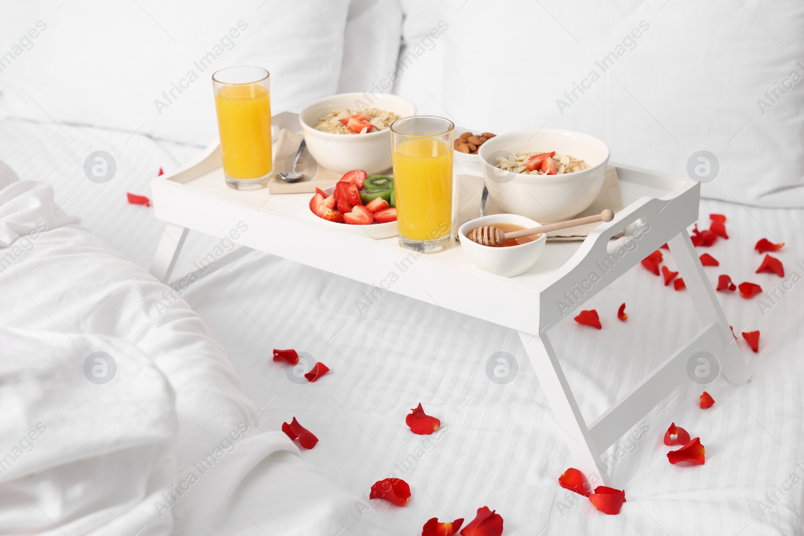 Tray with tasty breakfast and rose petals on bed at home Photo of Tray with tasty breakfast and rose petals on bed at home