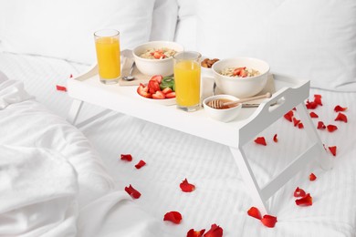 Photo of Tray with tasty breakfast and rose petals on bed at home