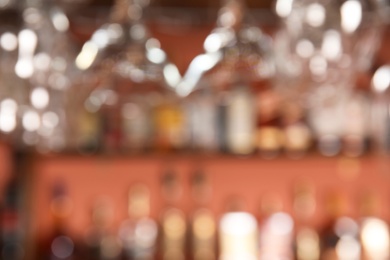 Photo of Blurred view of shelves with alcohol drinks and glasses in bar