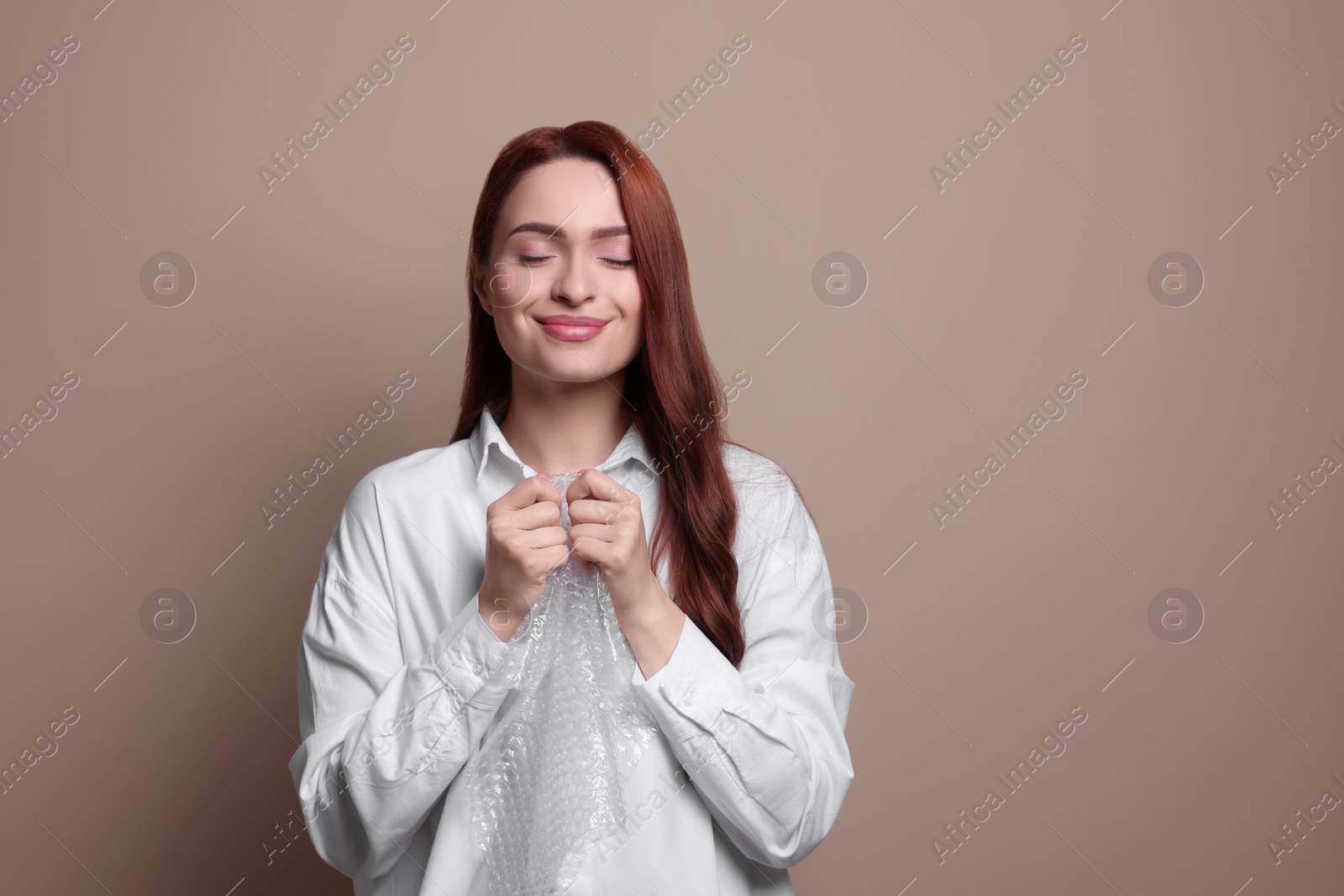 Photo of Woman popping bubble wrap on beige background, space for text. Stress relief