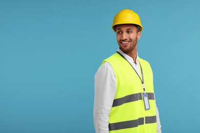 Engineer with hard hat and badge on light blue background, space for text