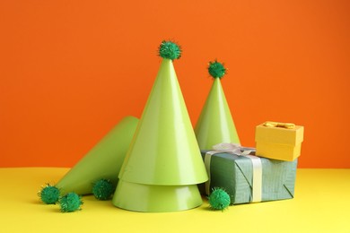 Party hats and gift boxes on yellow table against orange background