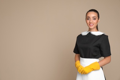 Portrait of young chambermaid in tidy uniform on color background