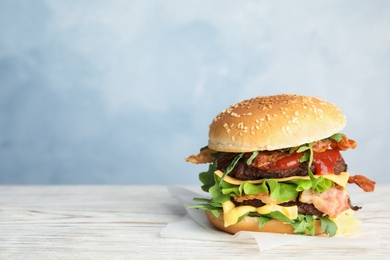 Tasty burger with bacon on table against color background. Space for text