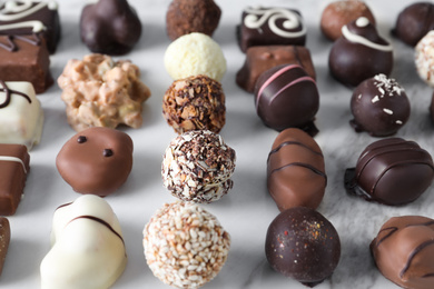 Photo of Different tasty chocolate candies on white marble table