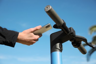 Photo of Man using smartphone to pay and unblock rental electric scooter outdoors, closeup