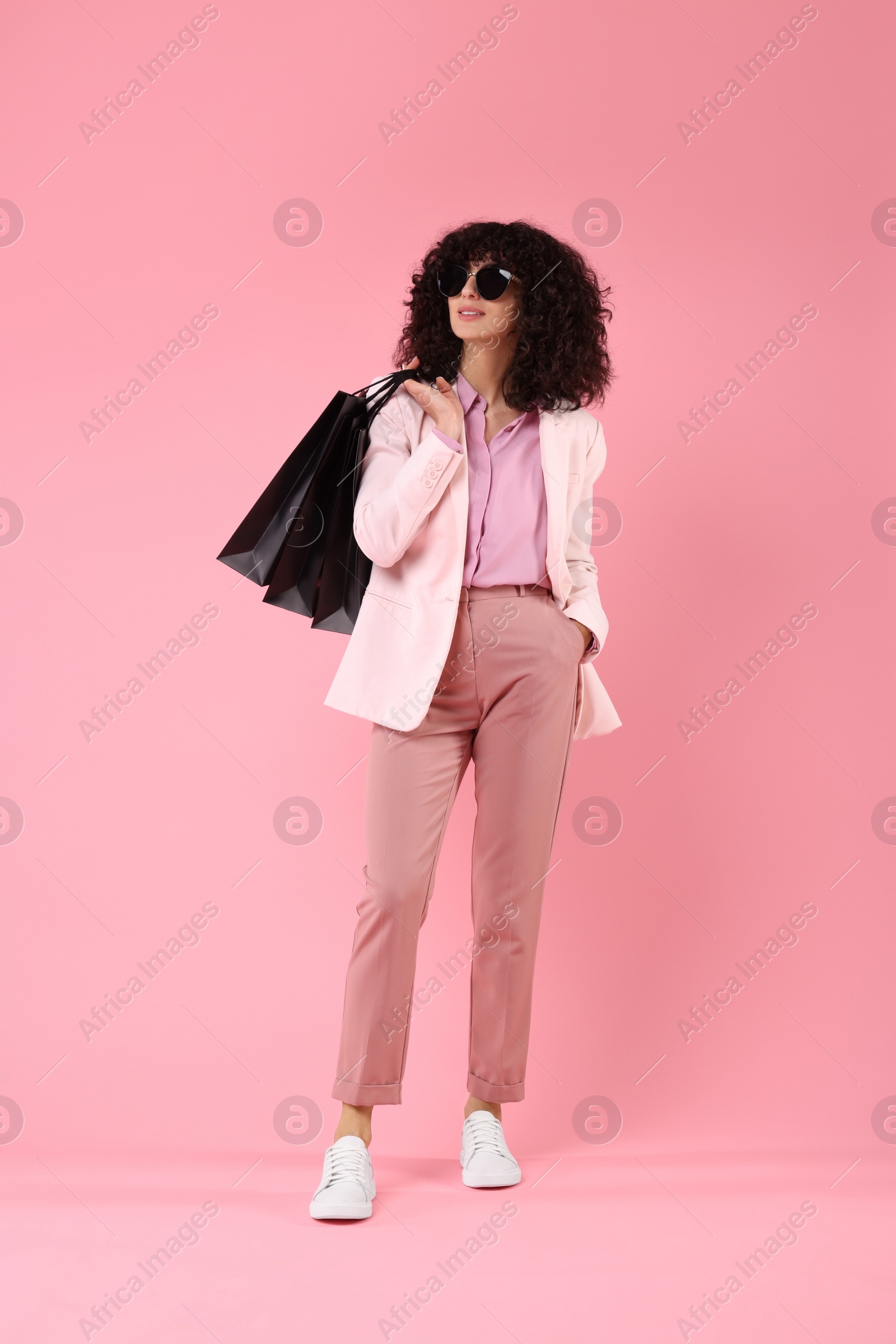 Photo of Happy young woman with shopping bags and stylish sunglasses on pink background