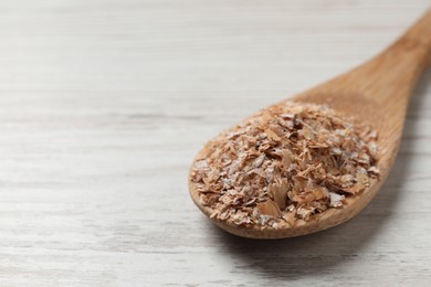 Spoon of wheat bran on white wooden table, closeup. Space for text