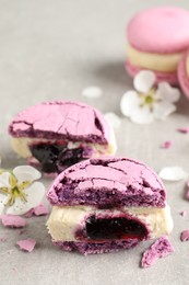 Photo of Halves of delicious violet macaron and flowers on light grey table