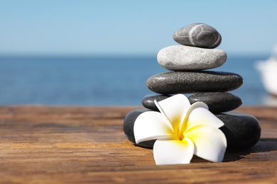 Photo of Stack of stones and flower on wooden pier near sea, space for text. Zen concept