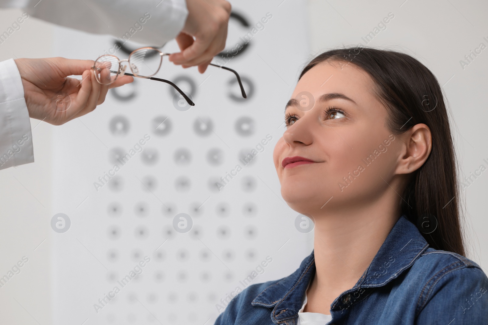 Photo of Vision testing. Ophthalmologist giving glasses to young woman indoors