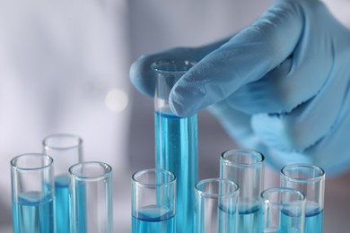 Scientist taking test tube with light blue liquid in laboratory, closeup