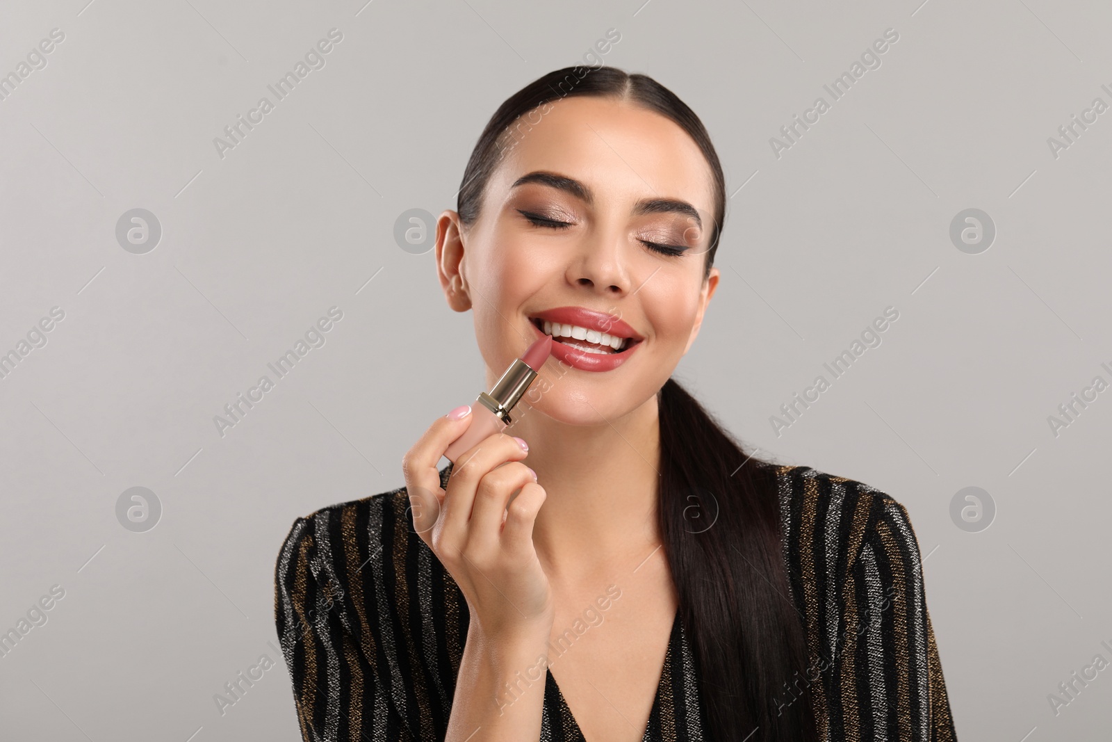 Photo of Everyday makeup. Beautiful woman applying lipstick on light grey background