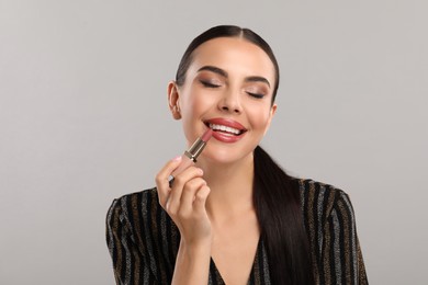 Everyday makeup. Beautiful woman applying lipstick on light grey background