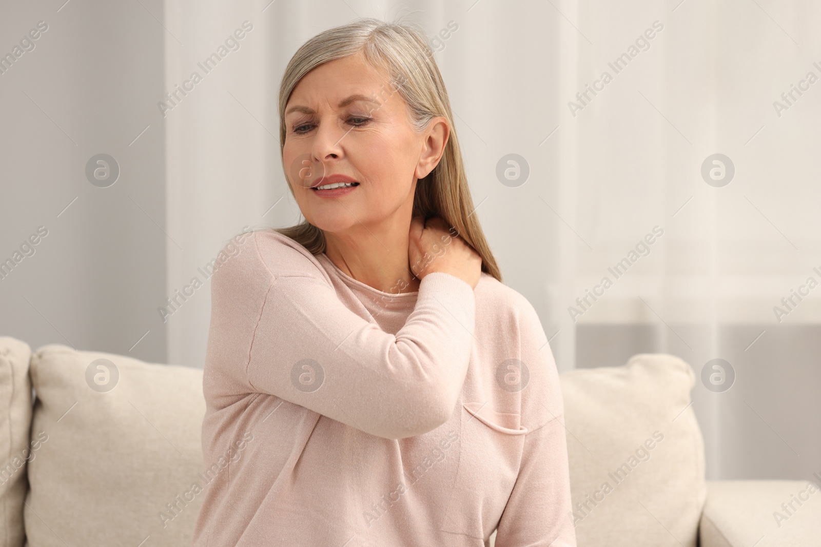 Photo of Mature woman suffering from pain in neck at home. Rheumatism symptom