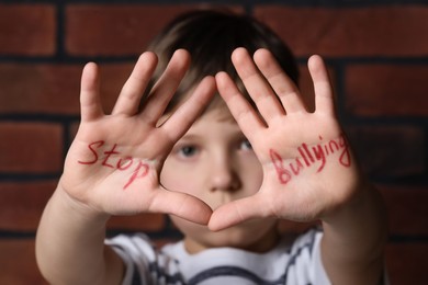 Photo of Kid showing hands with phrase Stop Bullying near brick wall, selective focus