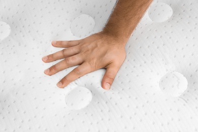 Young man touching modern orthopedic mattress, closeup