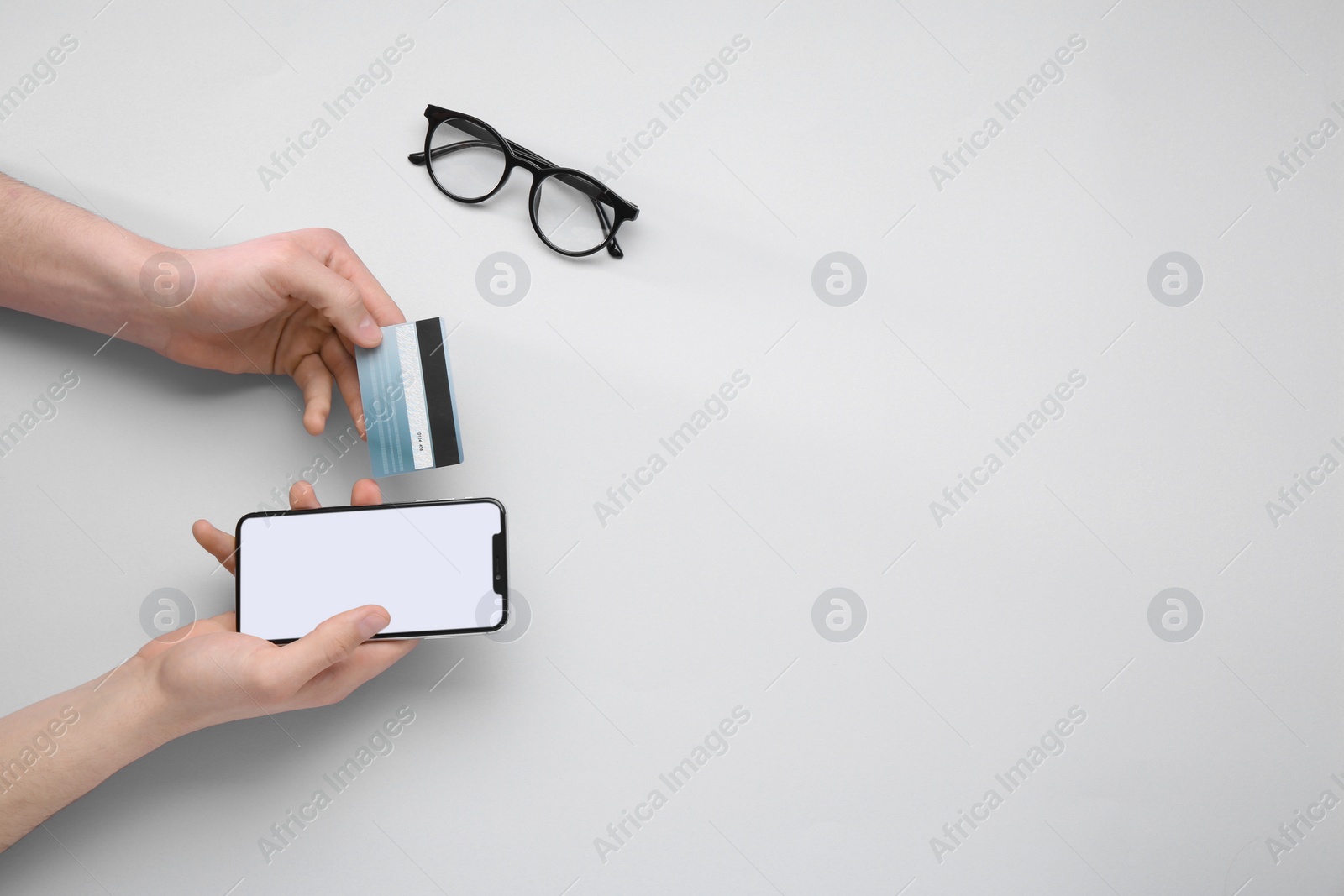 Photo of Online payment. Man with smartphone, credit card and glasses on light grey background, top view. Space for text