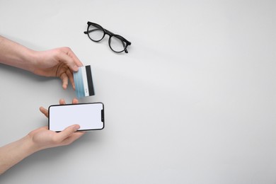 Photo of Online payment. Man with smartphone, credit card and glasses on light grey background, top view. Space for text