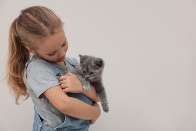 Cute little girl with kitten on light background, space for text. Childhood pet