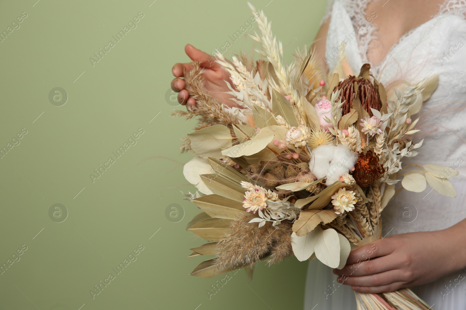 Photo of Bride holding beautiful dried flower bouquet on green background, closeup. Space for text