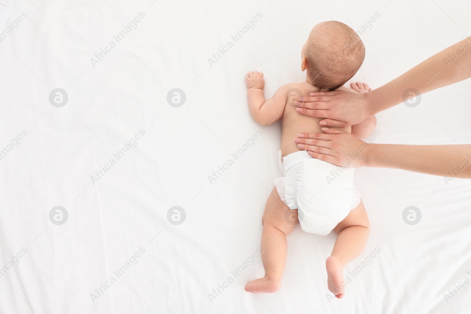 Photo of Top view of mother and her cute child on white bed, space for text. Baby massage and exercises