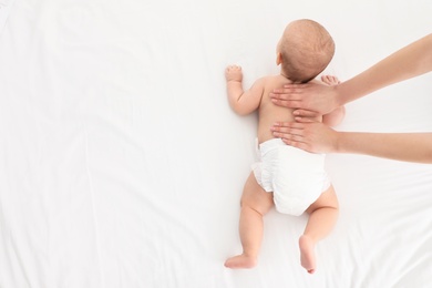 Photo of Top view of mother and her cute child on white bed, space for text. Baby massage and exercises