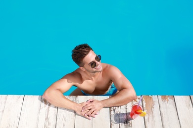 Handsome young man with refreshing cocktail in swimming pool on sunny day, above view