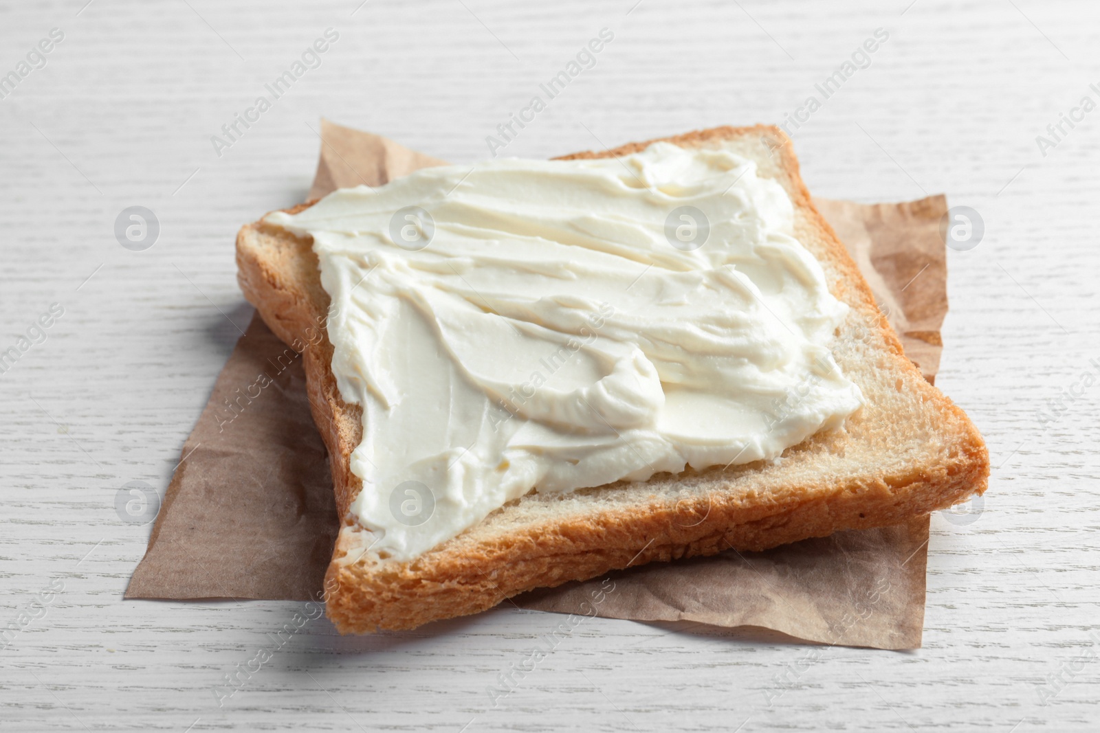 Photo of Slice of bread with tasty cream cheese on white wooden table, closeup