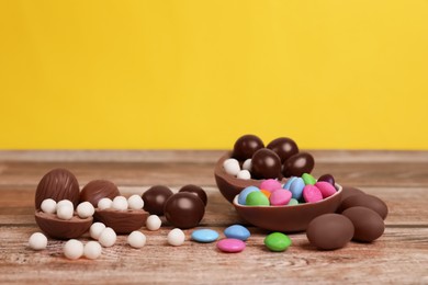 Photo of Delicious chocolate eggs and candies on wooden table against yellow background