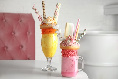 Photo of Tasty milk shakes with sweets in glassware on table at cafe