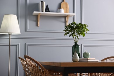 Photo of Vase with green branches, books and decor on wooden table in stylish dining room