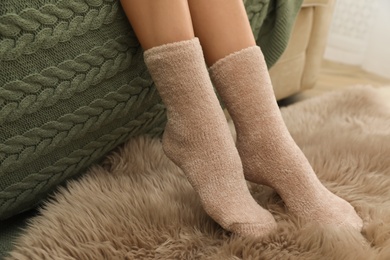 Photo of Woman in warm socks on sofa with knitted plaid, closeup