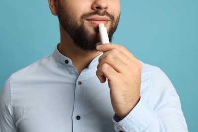 Photo of Young man applying lip balm on turquoise background, closeup