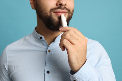 Young man applying lip balm on turquoise background, closeup