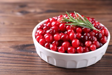 Fresh ripe cranberries and rosemary in bowl on wooden table, closeup