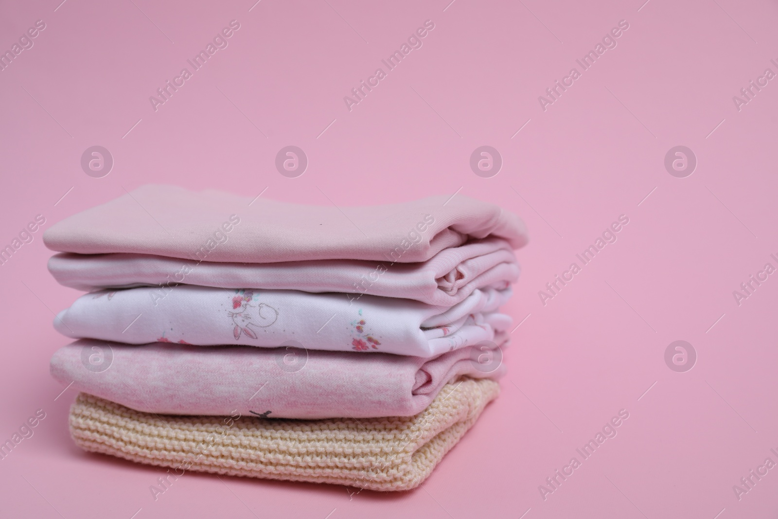 Photo of Stack of clean baby clothes on pink background. Space for text