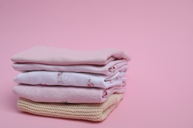 Stack of clean baby clothes on pink background. Space for text