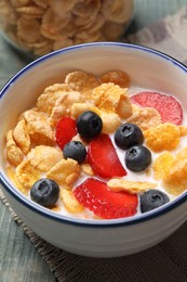 Photo of Delicious crispy cornflakes with milk and fresh berries on light blue wooden table, closeup