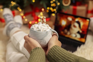 Photo of Woman drinking delicious cocoa and watching Christmas movie at home, closeup