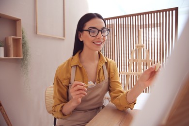 Photo of Young woman drawing on canvas with pencil at table indoors