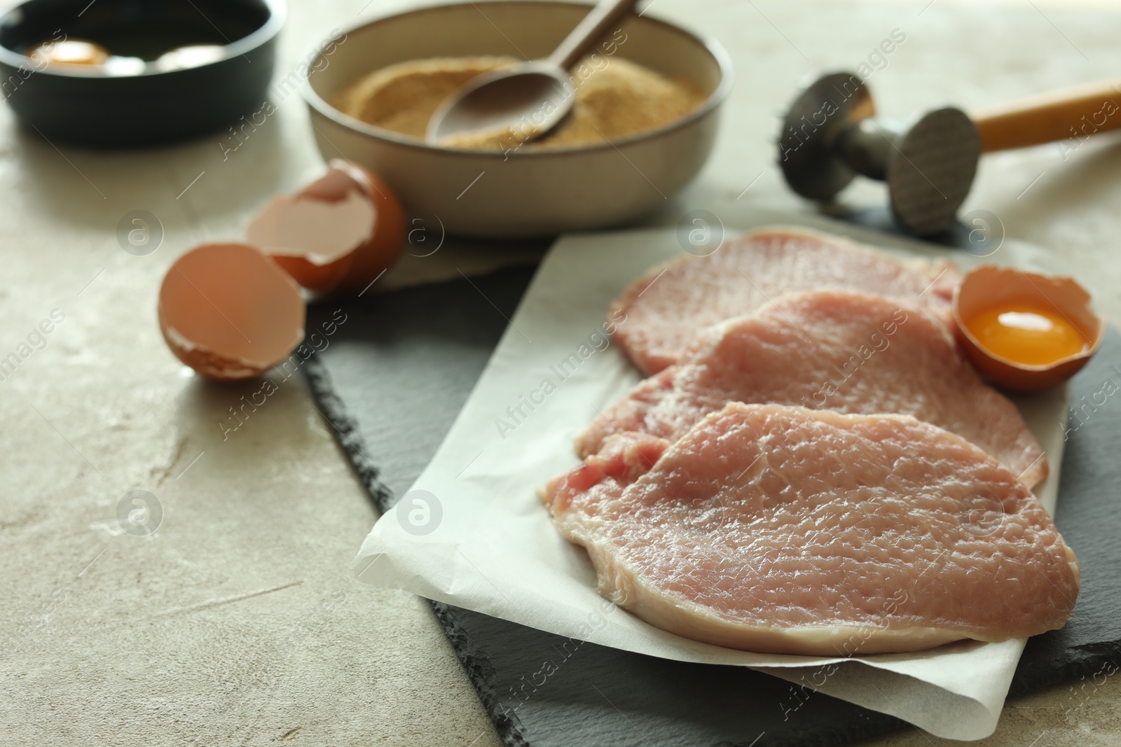 Photo of Cooking schnitzel. Raw pork chops, meat mallet and ingredients on grey table