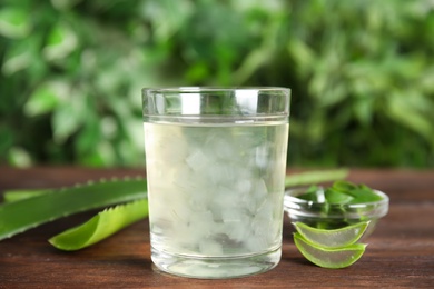 Photo of Fresh aloe drink in glass and leaves on wooden table