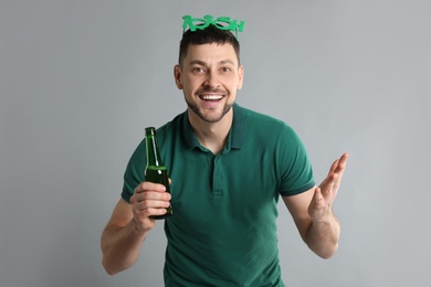 Happy man in St Patrick's Day outfit with beer on light grey background
