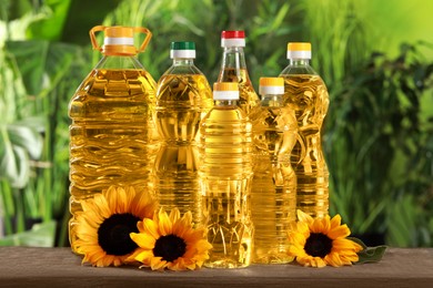 Photo of Bottles of cooking oil and sunflowers on wooden table against blurred background