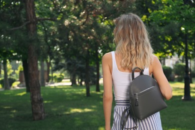 Photo of Young woman with stylish backpack in park, back view. Space for text