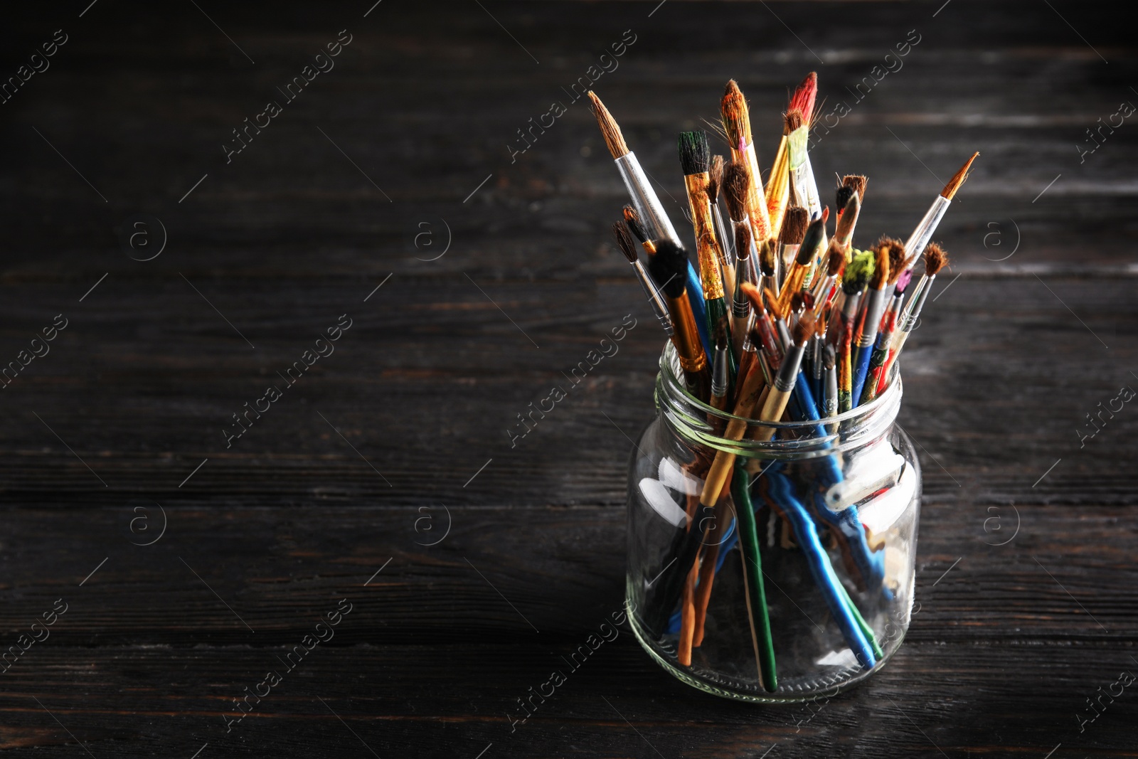 Photo of Jar with paint brushes on wooden table. Space for text