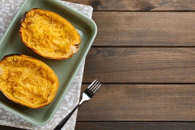 Photo of Halves of cooked spaghetti squash in baking dish and fork on wooden table, flat lay. Space for text