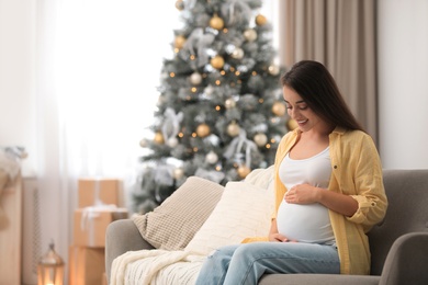 Photo of Happy pregnant woman on sofa in living room decorated for Christmas. Expecting baby