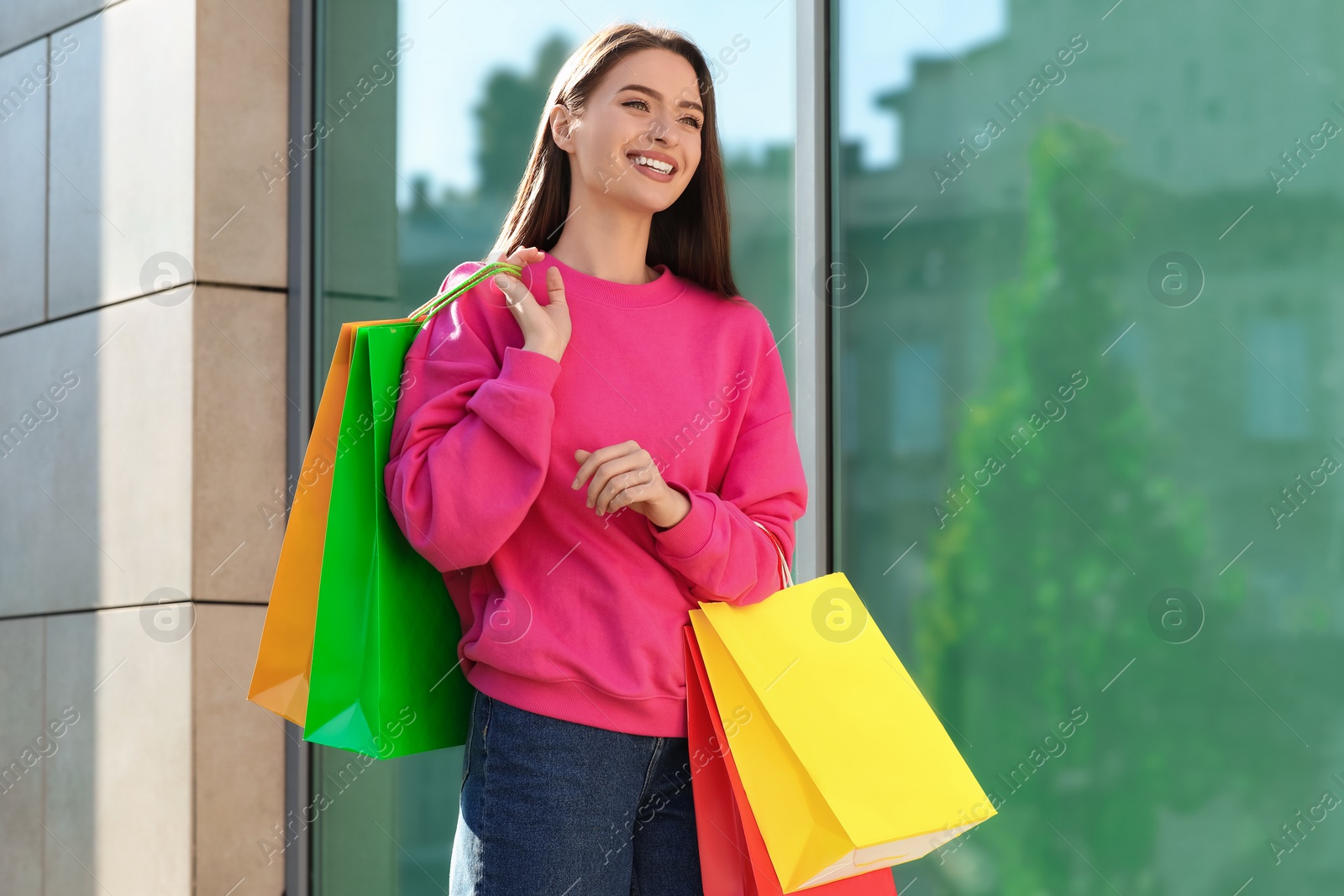 Photo of Beautiful young woman with shopping bags near building outdoors